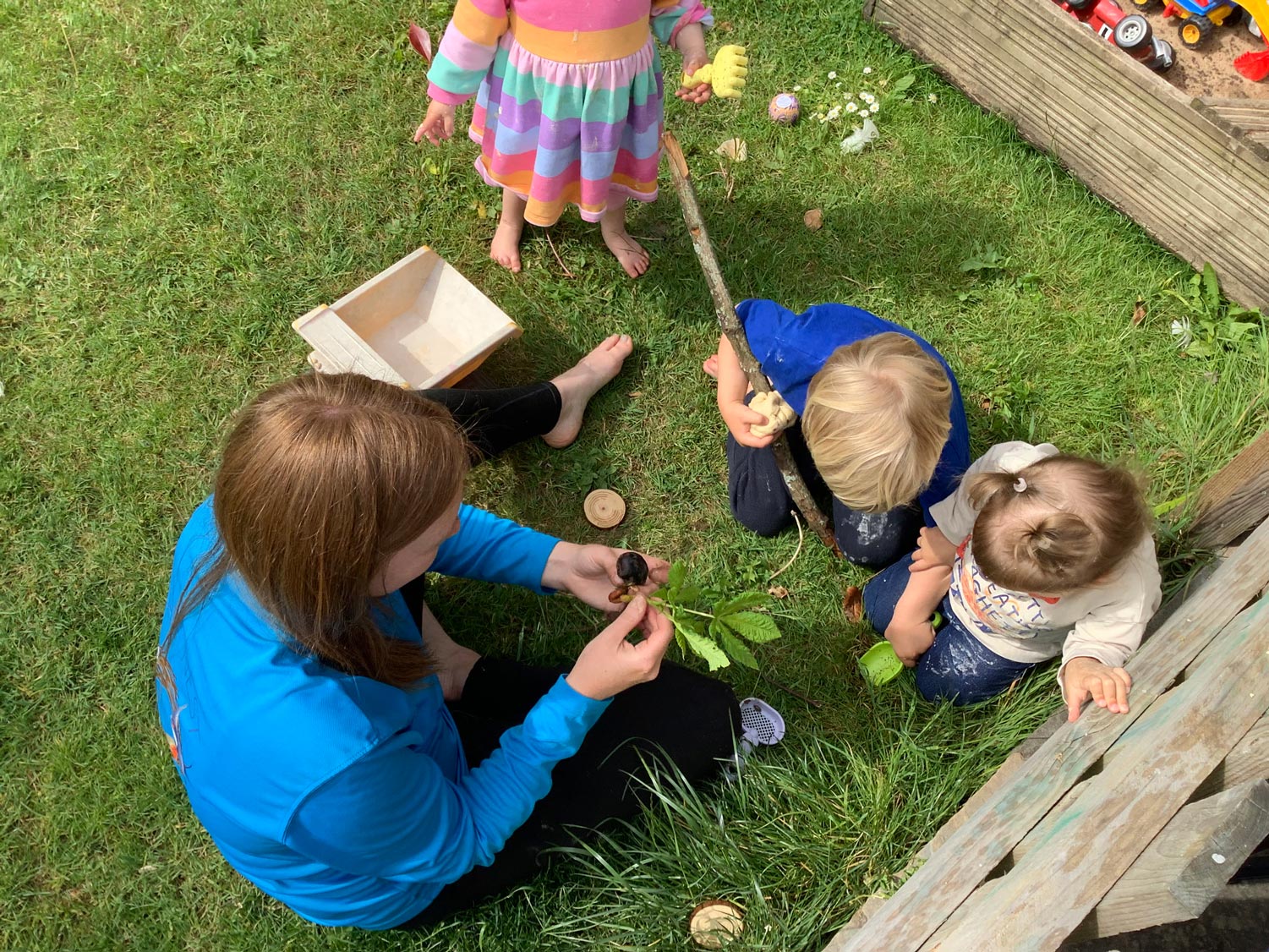 Nursery children exploring a snail and natural plant materials outdoors with an adult practitioner.