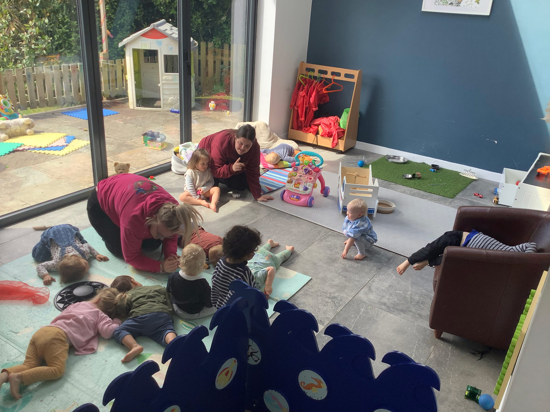 Nursery children lying on soft mats during a practitioner-led quiet story or sensory time indoors.