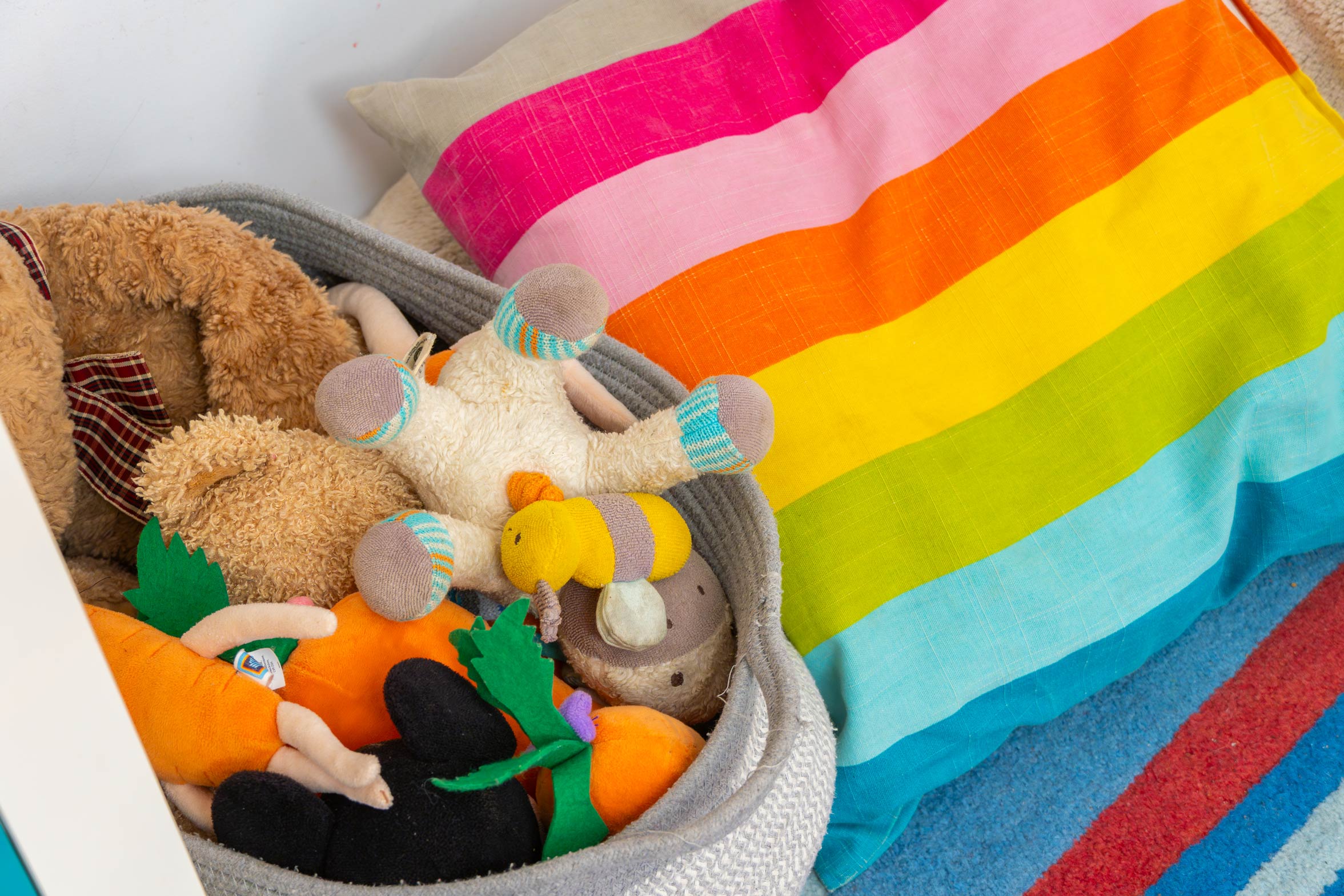 Basket of stuffed animals and teddys sat beside vibrant coloured pillow.
