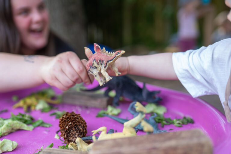 Child and Nest Team member playing outdoors with dinosaur toys.